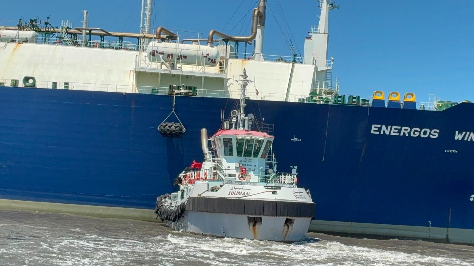 Tug Hedaya on the port bow of Energos Winter. Names visible on both hulls. Assist / refloat. Not the 29 July fire.