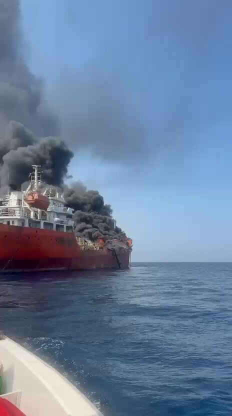 Poster. Small open boat beside a red-hulled tanker on fire. Stern painted PETRO DOLPHI….